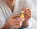 A person applying yellow nail treatment from a small bottle, focusing on nail care in a home setting.