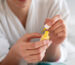 A person applying yellow nail treatment from a small bottle, focusing on nail care in a home setting.
